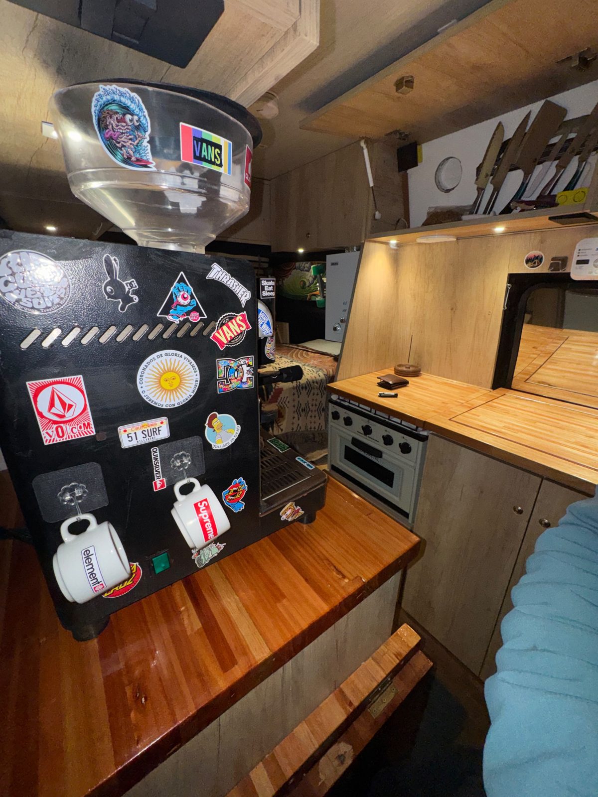 La cafetera de una boca instalada sobre la mesada de madera dentro de la van, con dos tazas colgadas